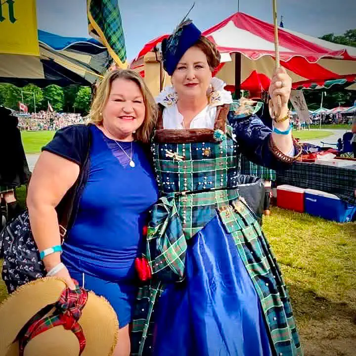 Two people at an outdoor Highland event, with a tartan and blue dress on display.